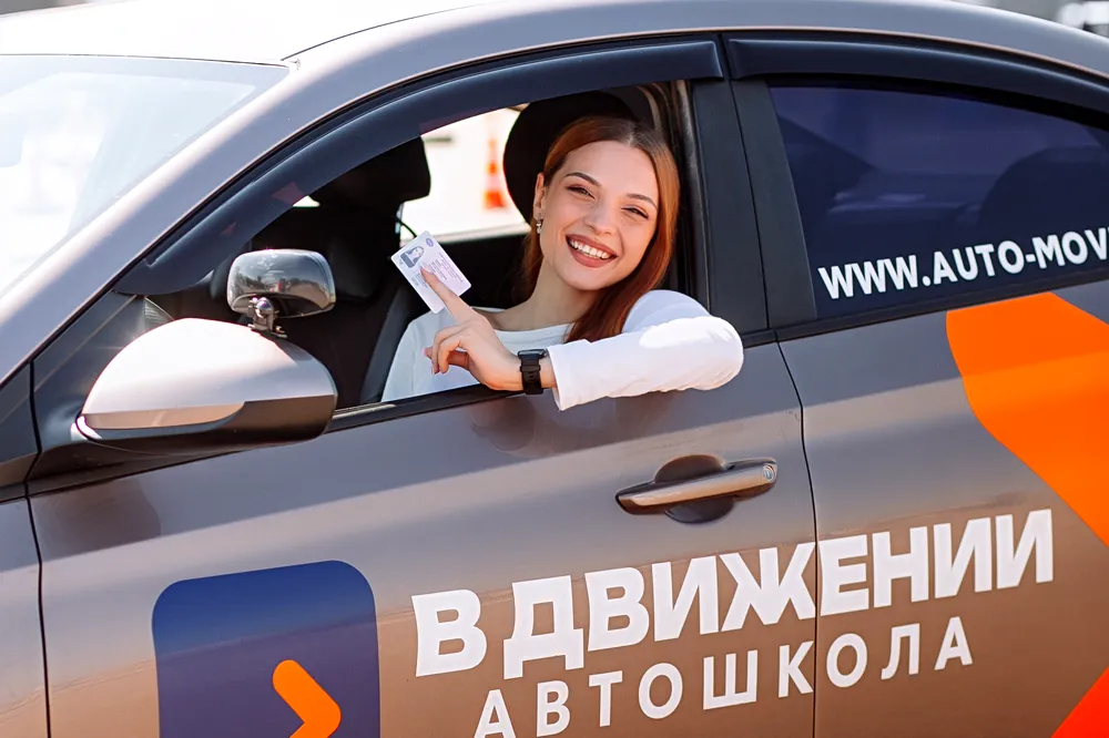 Выпускница показывает права из окна учебной машины